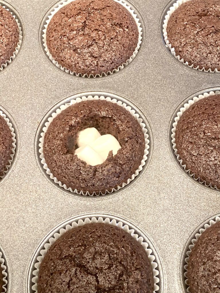 Closeup of one cupcake cut open with marshmallows inside of it before going back into the oven