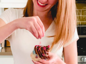woman with red hair putting sprinkles on a cupcake