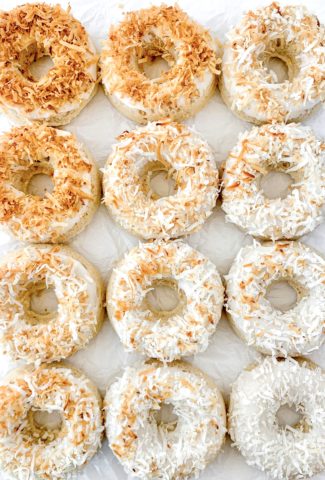 One dozen donuts arranged with a color gradient from dark brown toasted coconut flakes on top to white untoasted coconut flakes on top