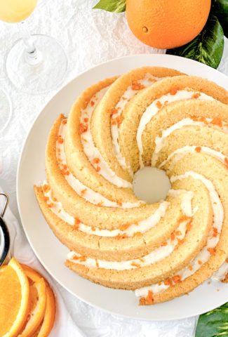 Decorative photo of the bundt cake covered in icing, orange zest, and surrounded by glasses of mimosas and oranges