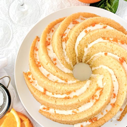 Decorative photo of the bundt cake covered in icing, orange zest, and surrounded by glasses of mimosas and oranges
