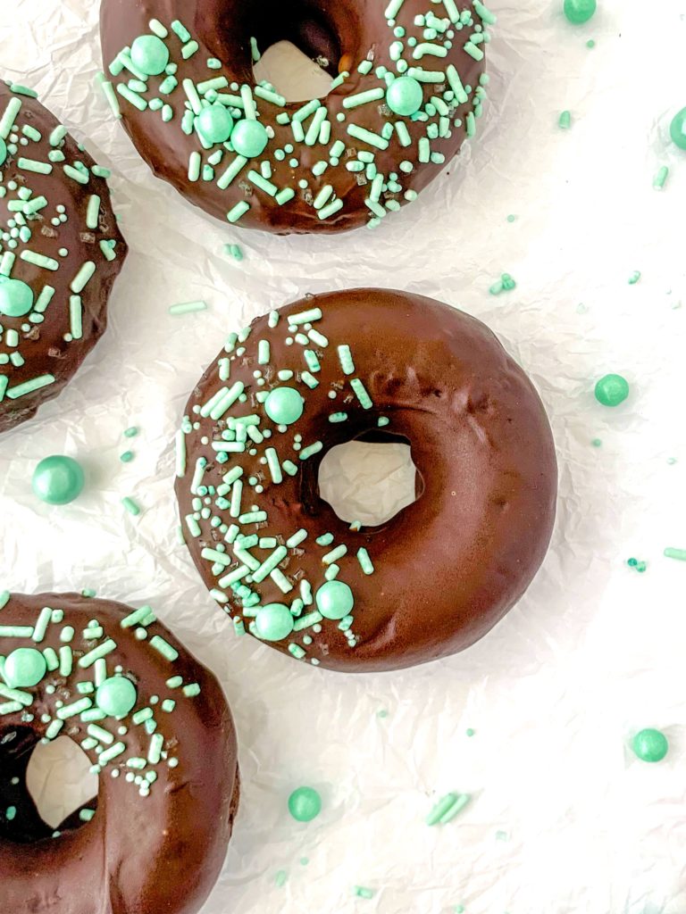A few donuts on a white backdrop with green sprinkles