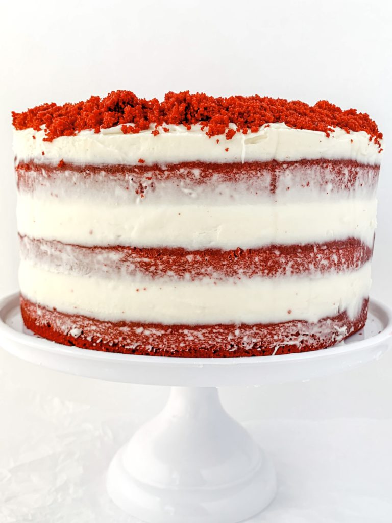 Photo of a completed red velvet cake on a cake stand, covered in frosting and cake crumbs on top