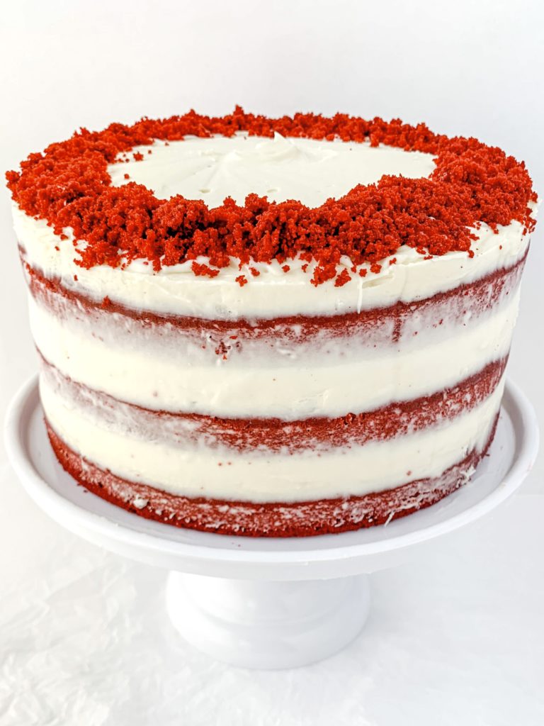 Photo of a completed red velvet cake on a cake stand, covered in frosting and cake crumbs on top