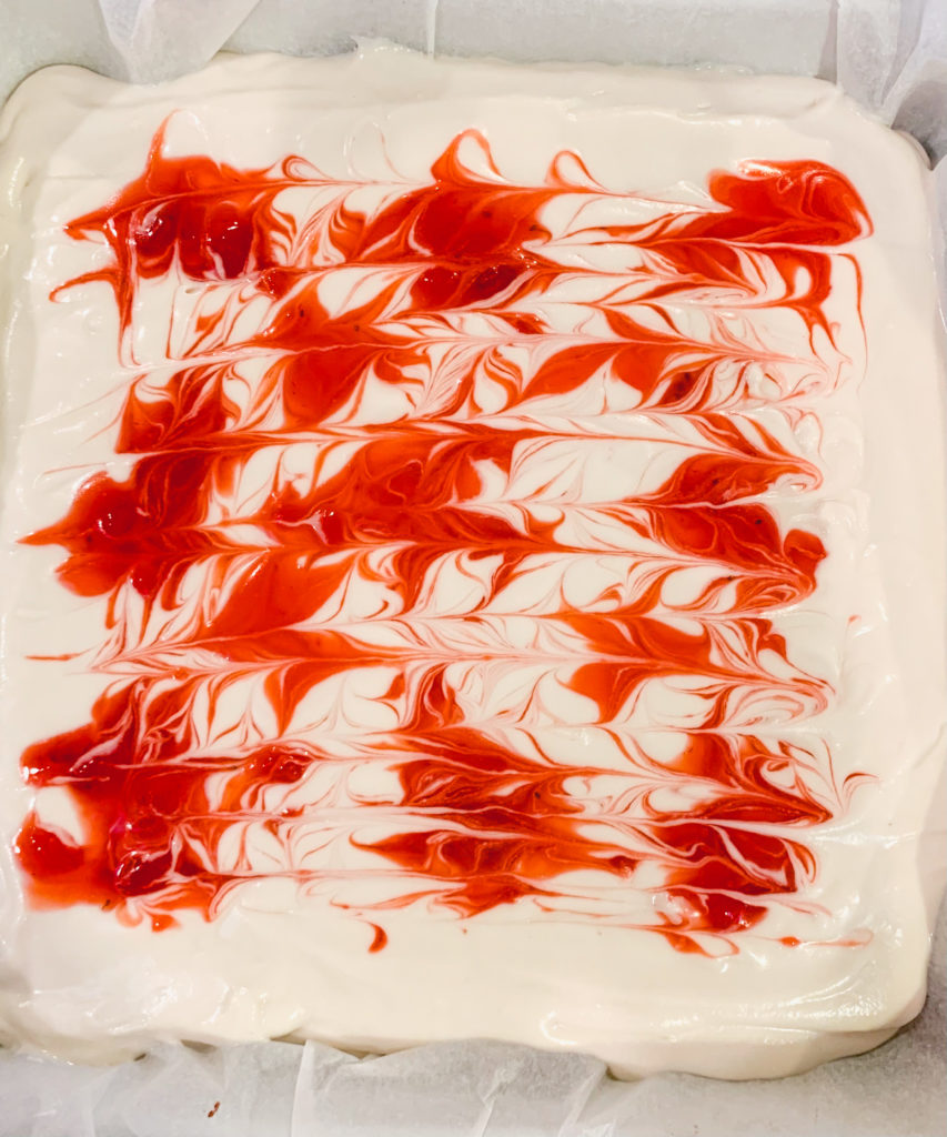 Swirl of strawberry sauce on top of cheesecake bars, unbaked