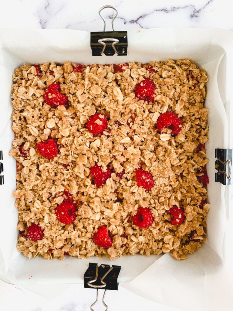 The whole thing put together in a pan, but unbaked. Photo is looking down on a parchment paper lined pan with crumble topping and fresh berries poking through