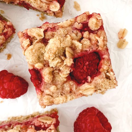 Close up of one bar on a white background with the crumble top and one raspberry poking through