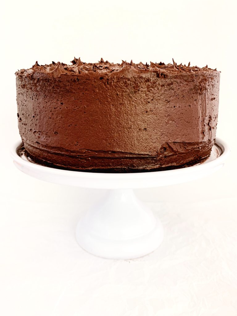 Completely frosted chocolate cake on a white cake stand
