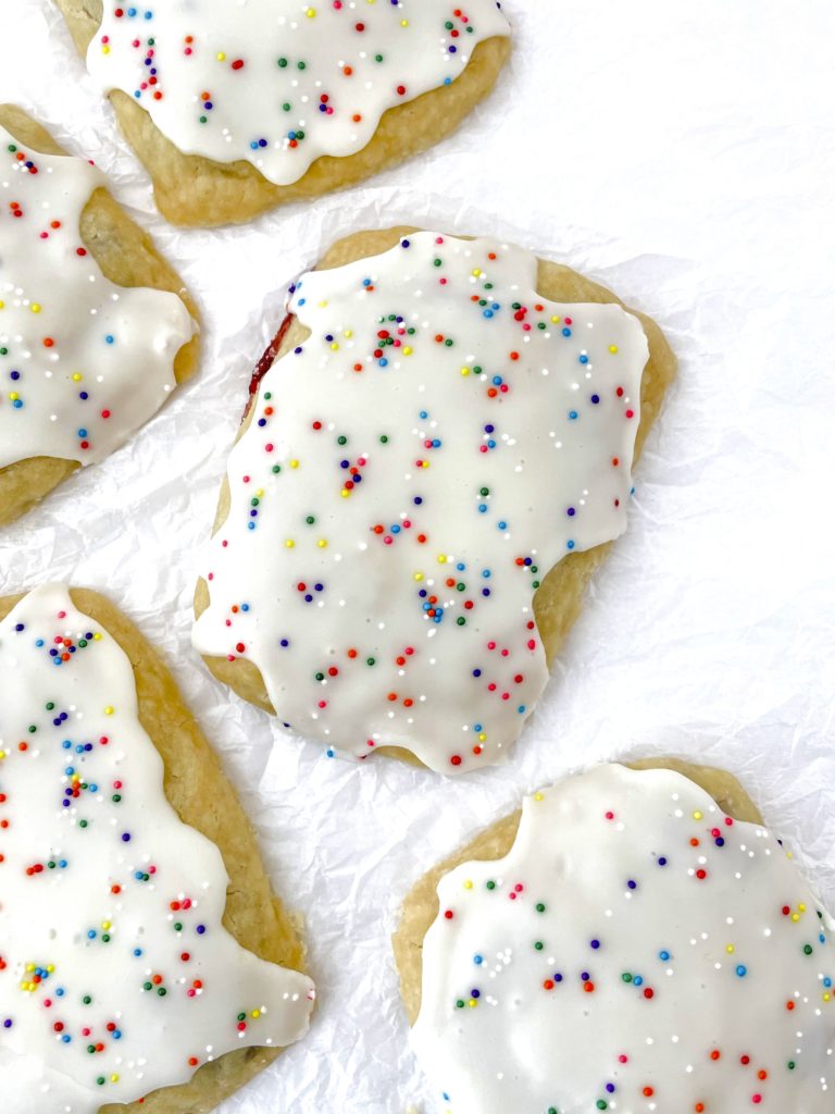 Photo looking down on a bunch of homemade vegan pop tarts all covered with a white icing and rainbow sprinkle balls