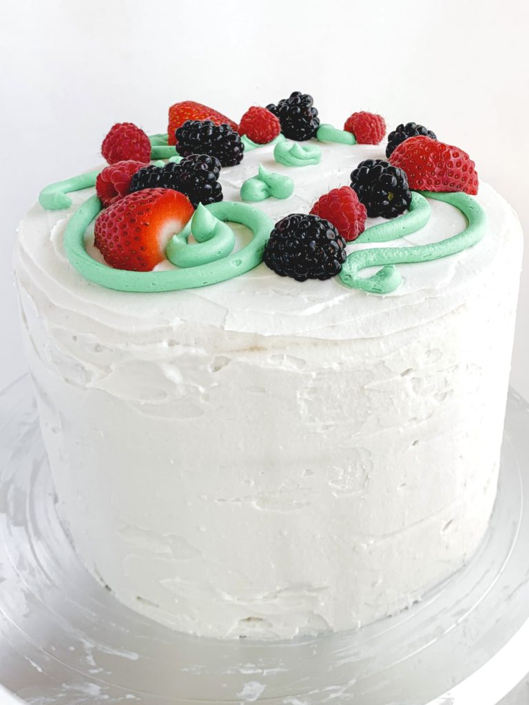 Photo of the completed cake decorated with fresh berries and cream buttercream swirls