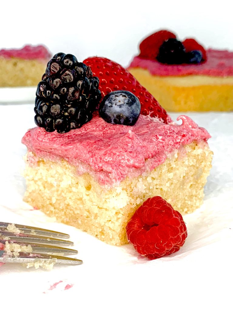One close up piece of cake with bright pink frosting, topped with a few fresh berries, on a white surface