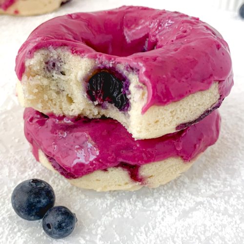Two donuts on top of each other, one with a bite taken out, both with a bright pink glaze