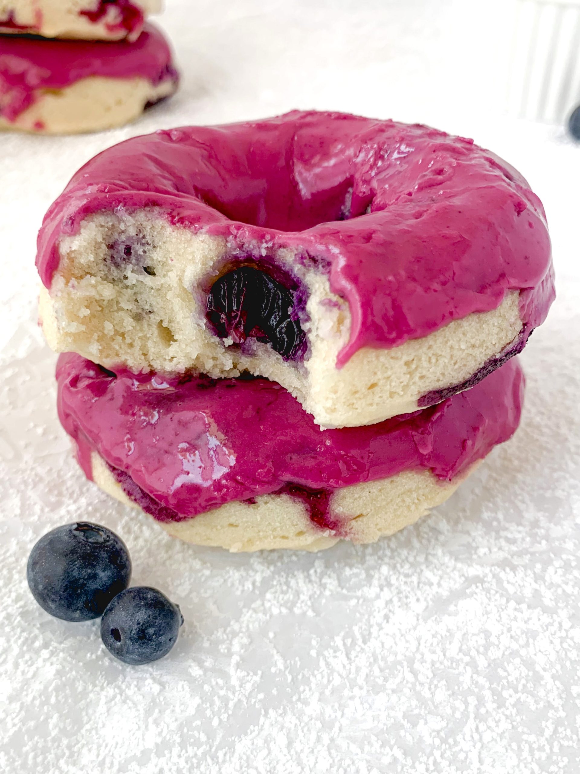 Two donuts on top of each other, one with a bite taken out, both with a bright pink glaze