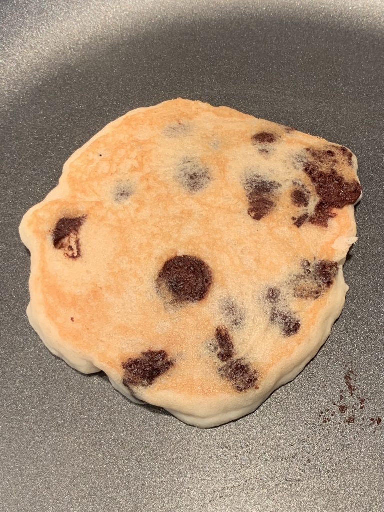 Chocolate chip pancake batter with the top side cooked, still on the pan