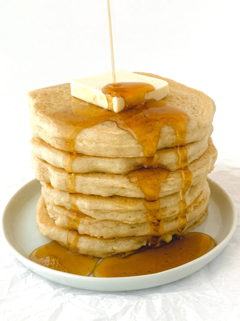 Stack of pancakes with a pat of butter on top and syrup drizzling down onto the pancakes
