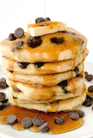Big stack of chocolate chip pancakes with syrup drizzling down on top of them
