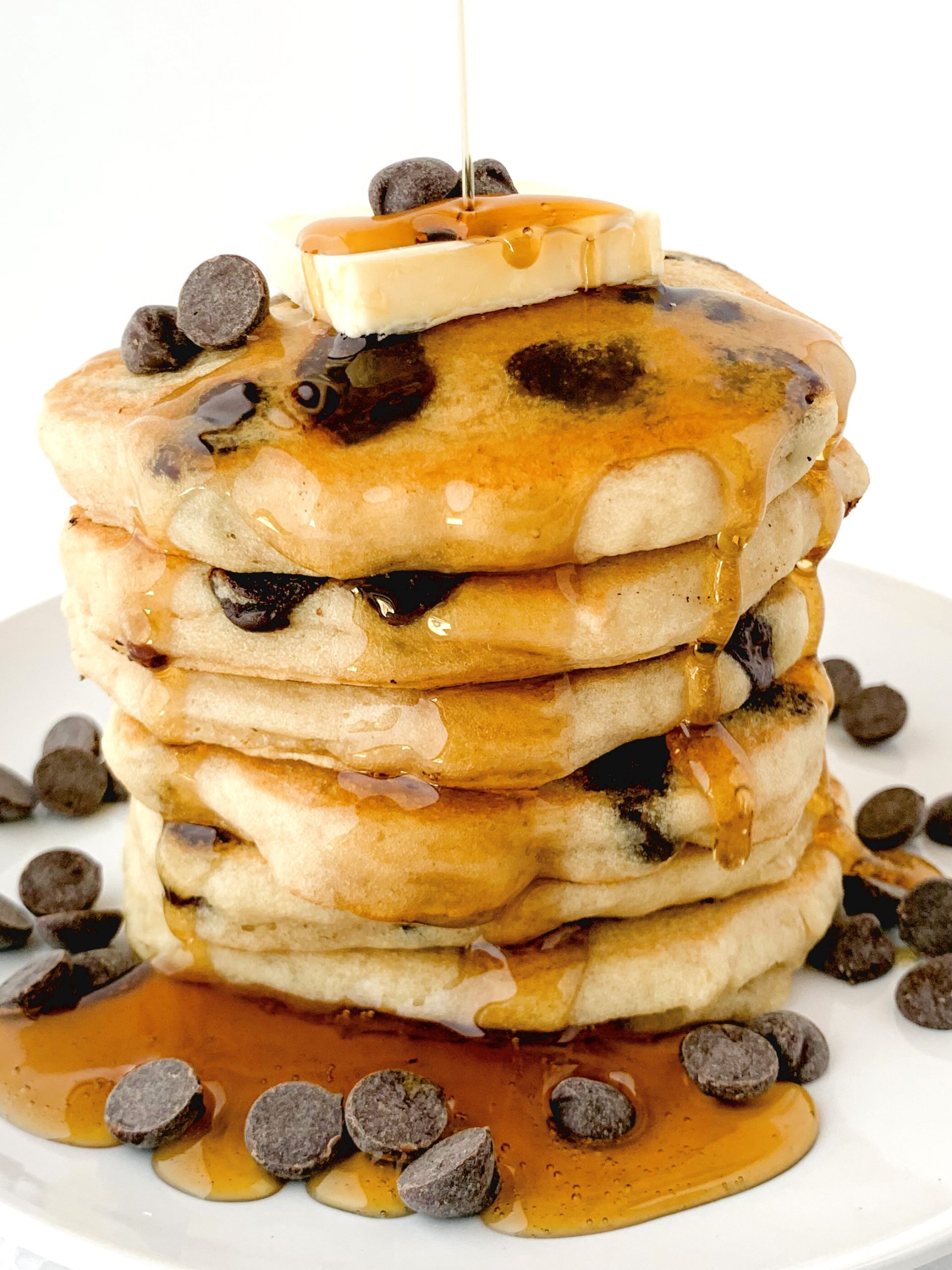 Big stack of chocolate chip pancakes with syrup drizzling down on top of them