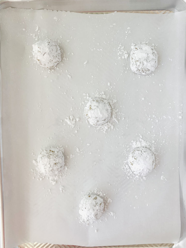 Uncooked balls of cookie dough covered in powdered sugar on a pan